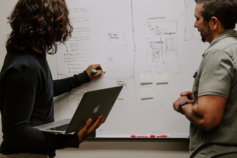 A PM writes on the white board while a colleague watches