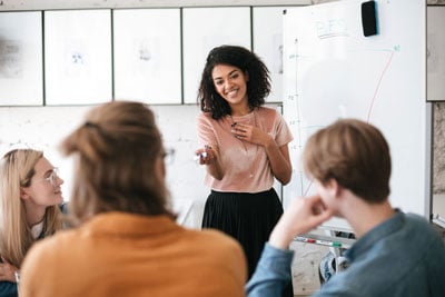 A young business woman standing in front of a flip chart leading a meeting with her team